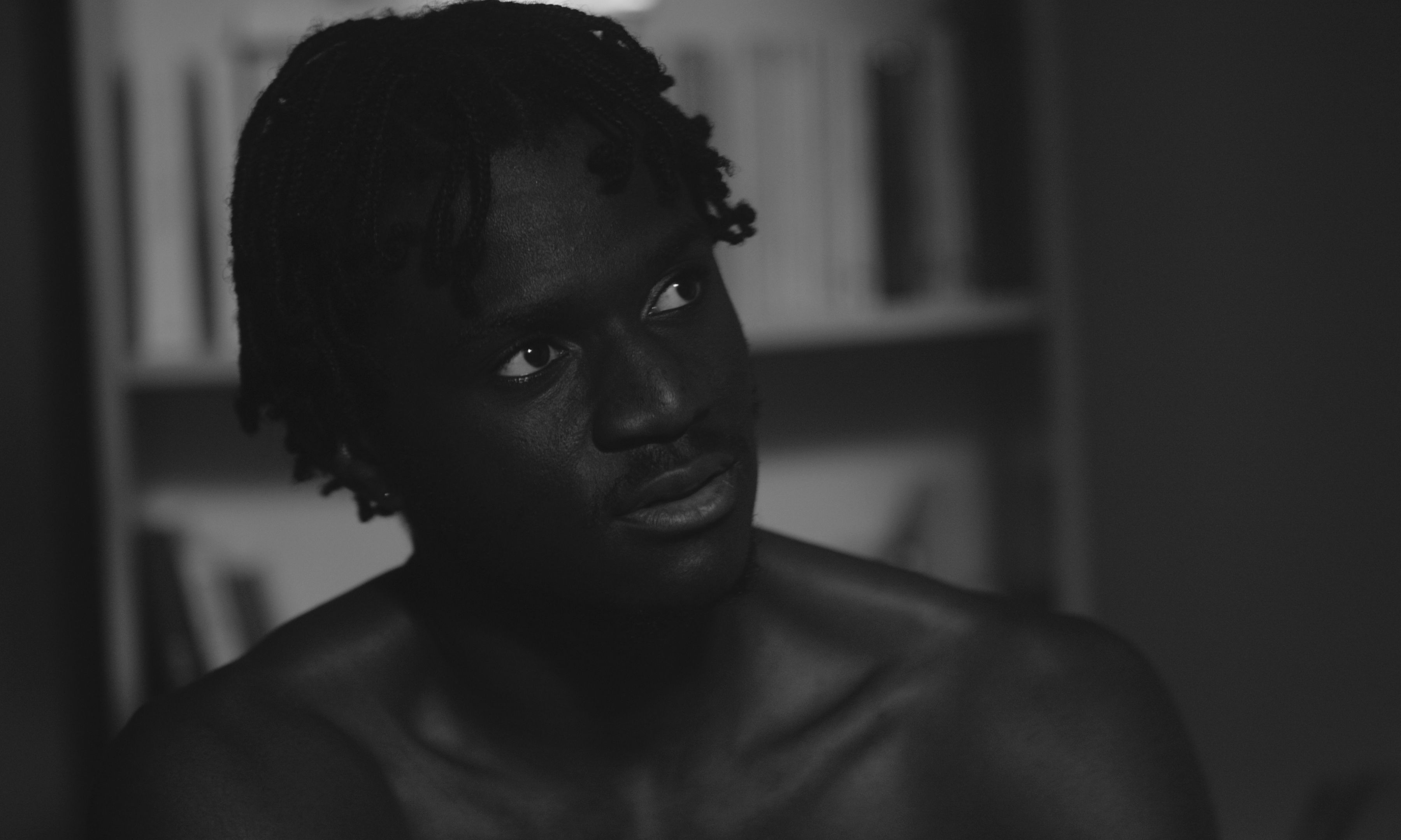 Photogramme du film Un Ange Aimé, en noir et blanc : un jeune homme dans une lumière de nuit, devant une bibliothèque.