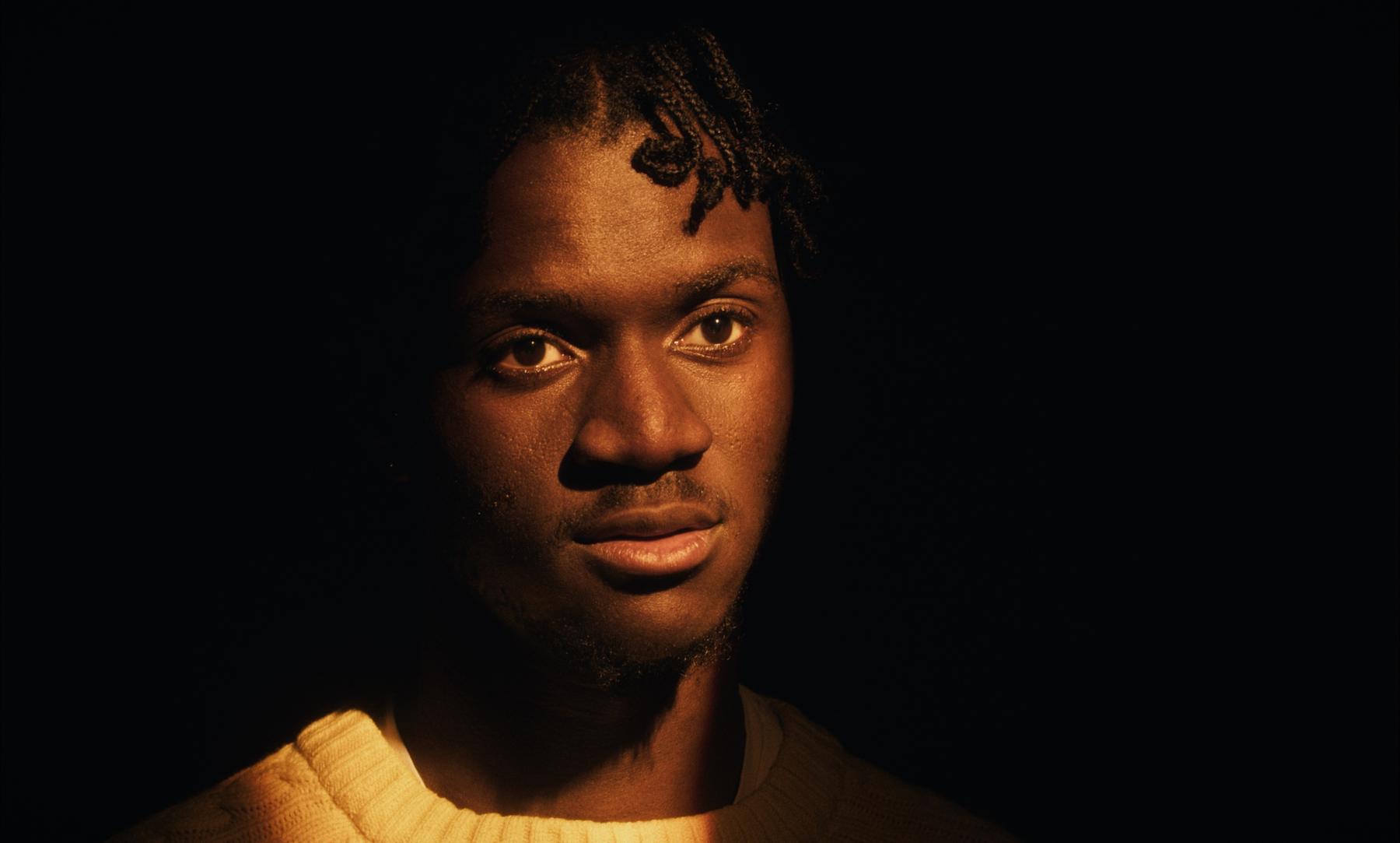 Photogramme : portrait d'un jeune homme en clair-obscur doré, face caméra.