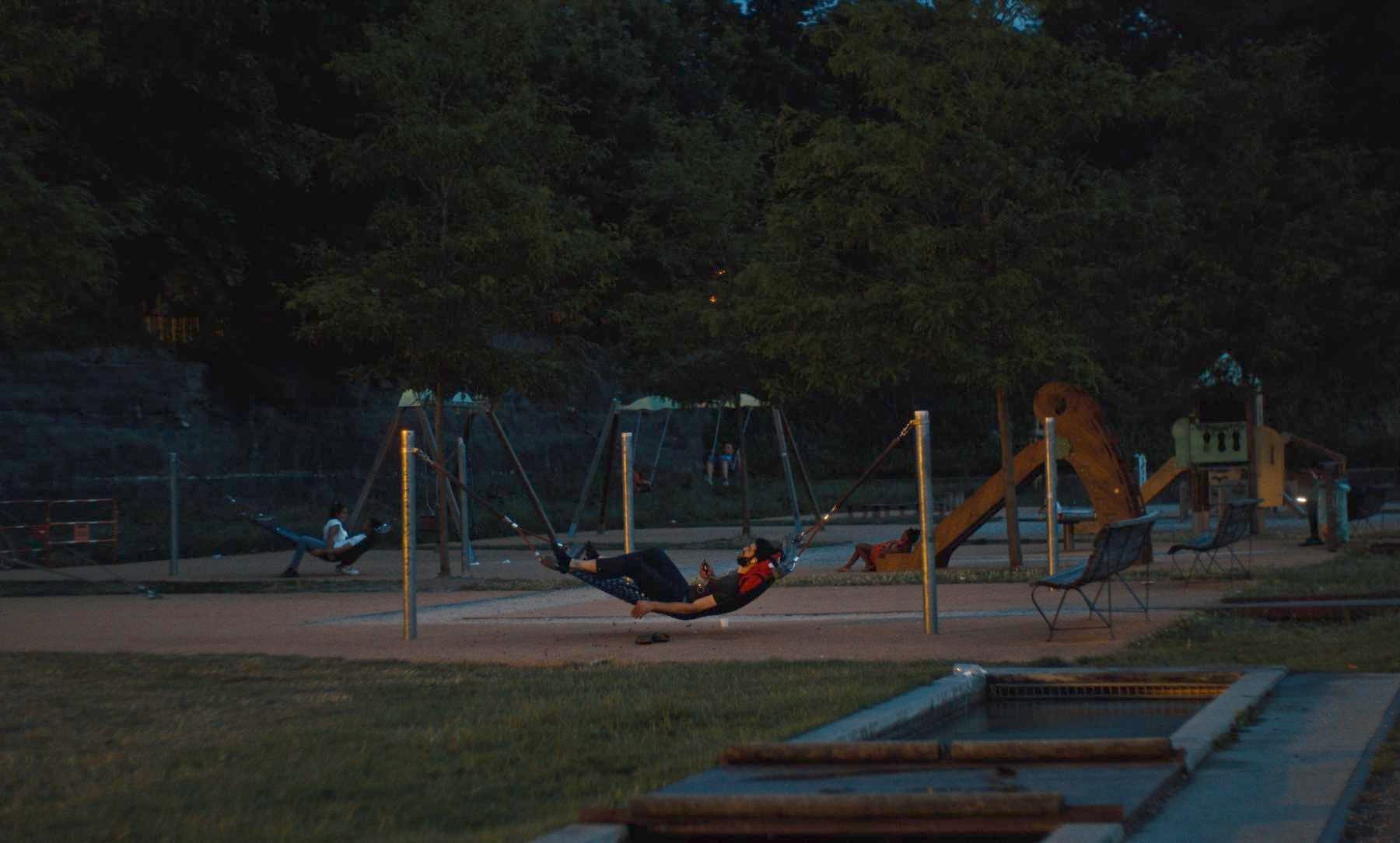 Photogramme de Sainté : un homme allongé dans un hamac d'aire de jeux, à la tombée de la nuit.