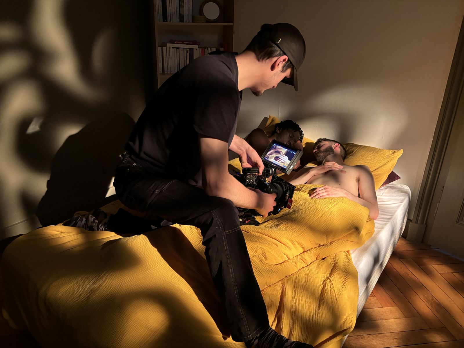 Sur le plateau : le chef opérateur filme une scène de lit dans une lumière dorée.